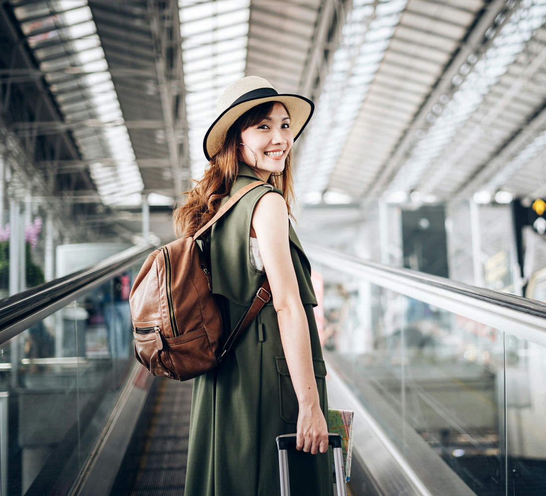 Junge Frau mit Sonnenhut zieht einen Reisekoffer hinter sich her
